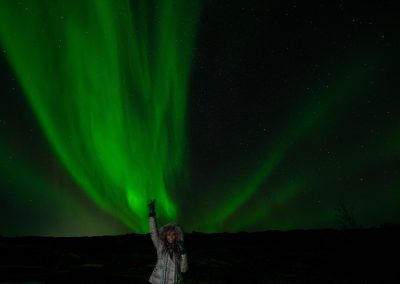 Guest standing beneath green Northern Lights in Iceland