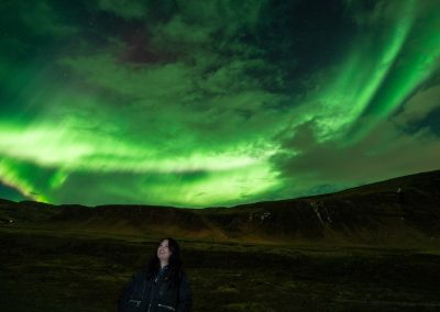 Guest under bright green Northern Lights in Iceland