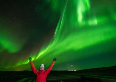 Guest celebrating beneath bright green Northern Lights